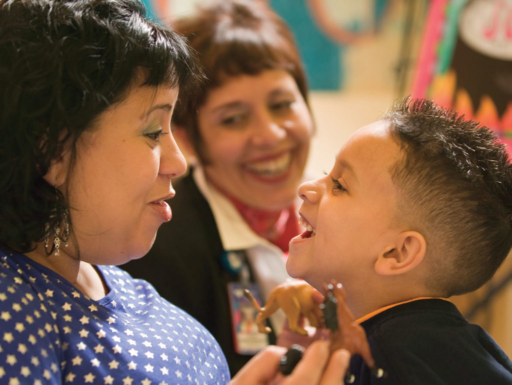 Laughing mother and young boy in a classroom with another woman smiling beyond