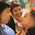 Laughing mother and young boy in a classroom with another woman smiling beyond