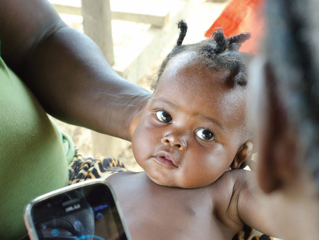 Baby with head supported being checked by phone by telemedicine health provider