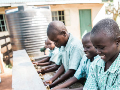 children in school uniforms watching their hands outside a school