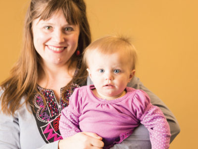 Smiling mother with a blond baby in a pink shirt