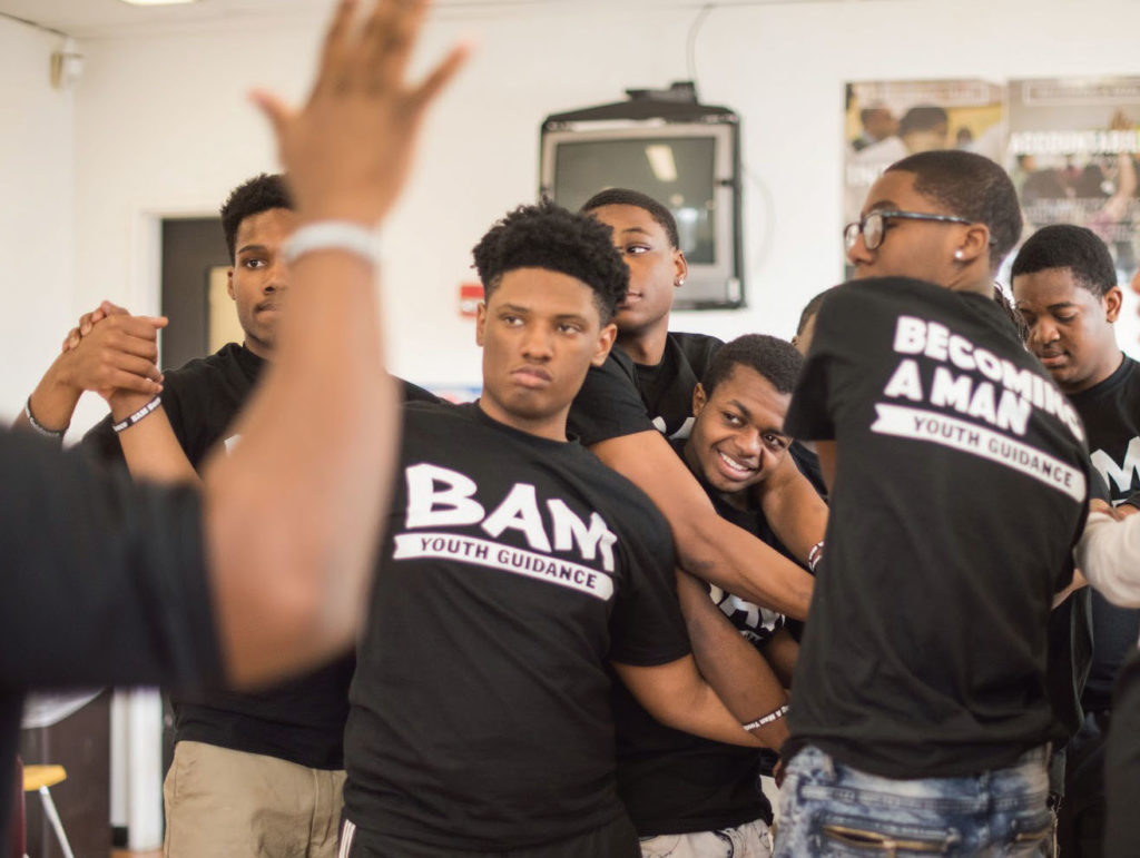 Young men wearing BAM, Becoming a Man, black t-shirts, embracing and clasping hands