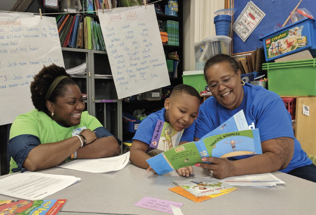 Two smiling woman working to teach a little boy to read