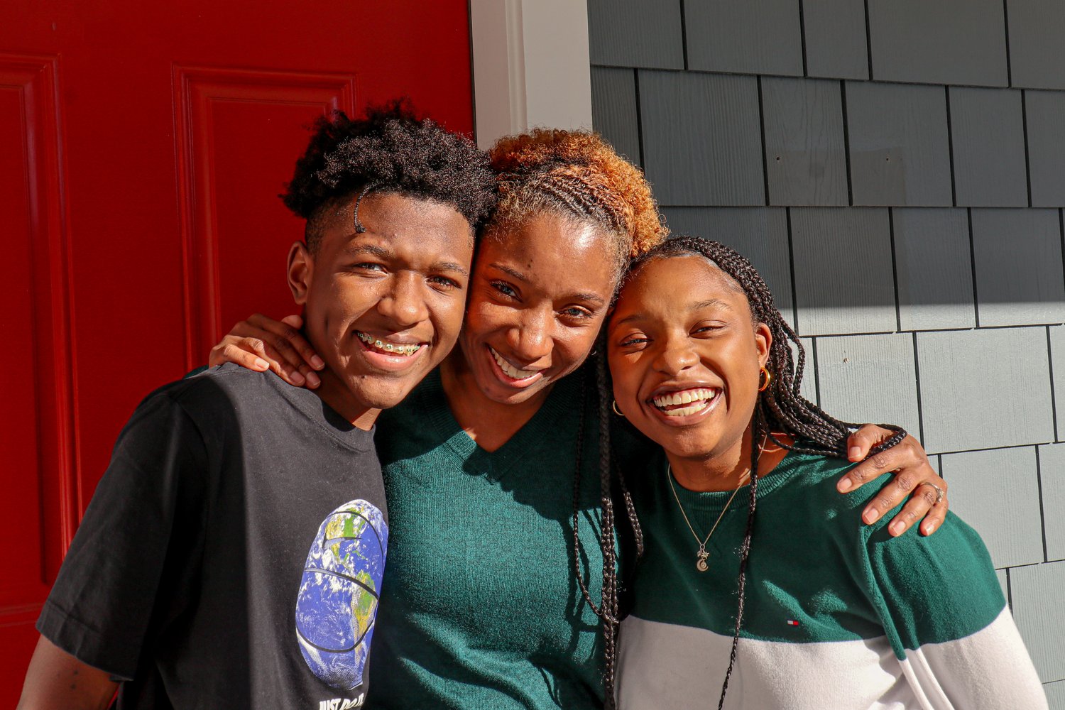 A mother and her two teenage children smiling on their porch