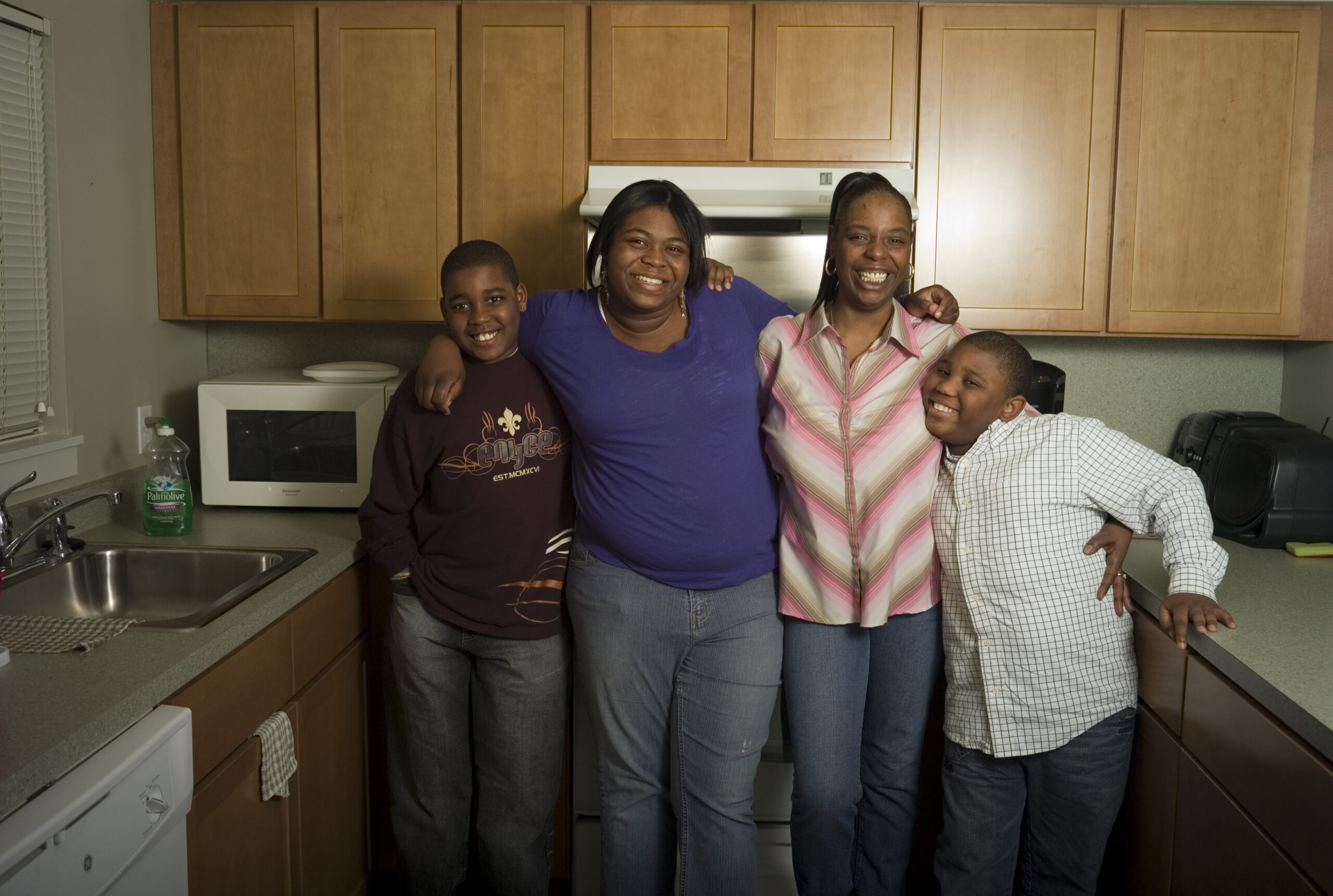 A family stands in their kitchen, smiling.