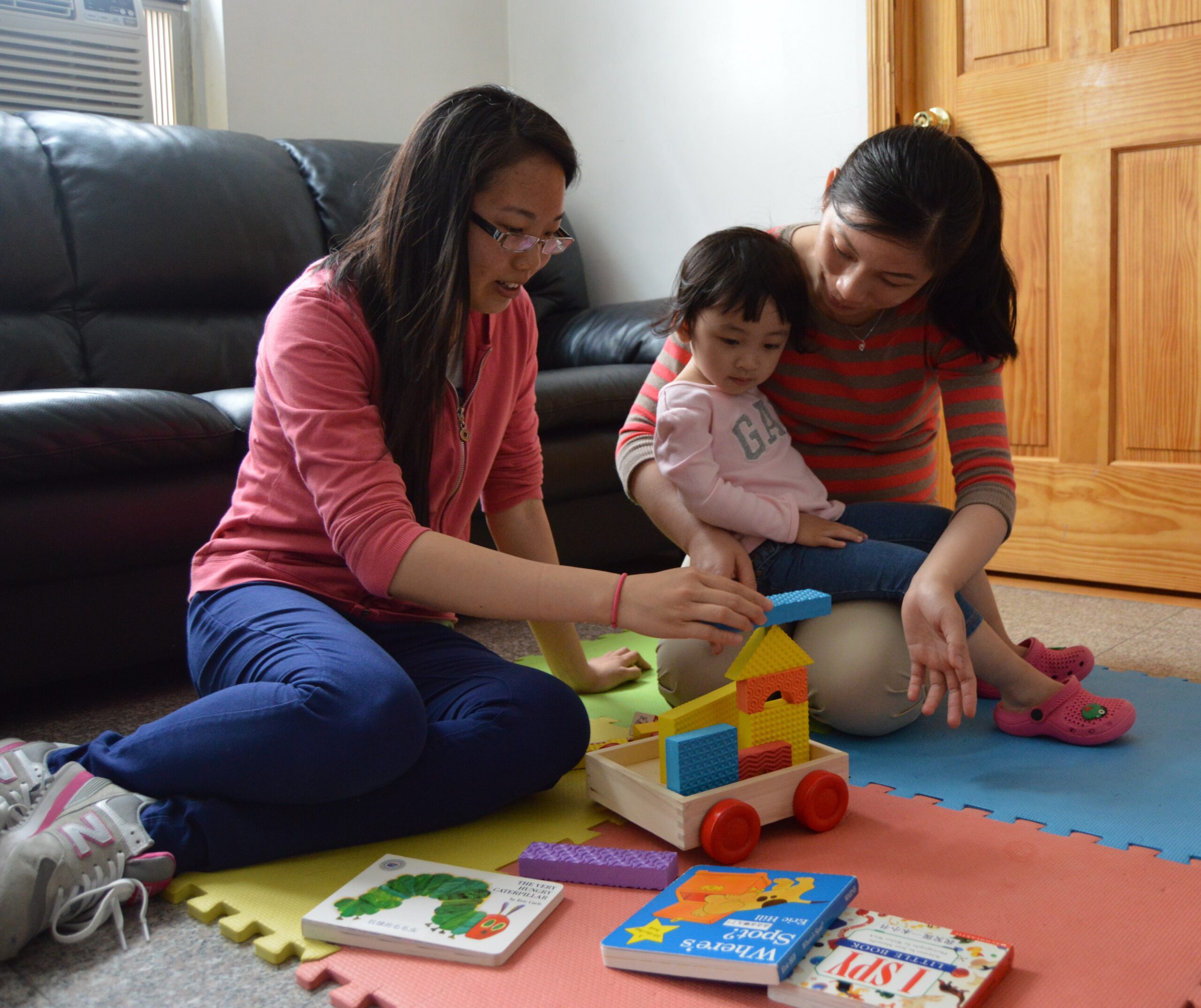 Two women play with a child in a living room.