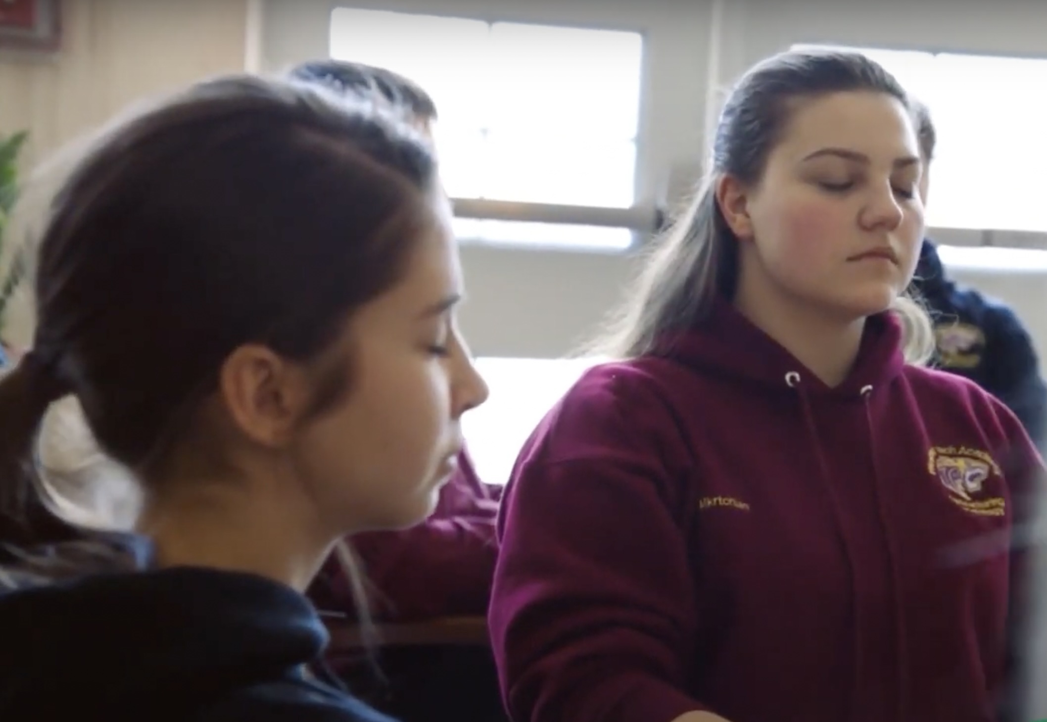 Two female students close their eyes while meditating.