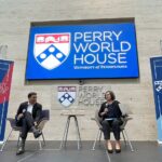 Rajiv Shah and Kat Rosqueta sit on a stage in front of a sign that says "Perry World House"