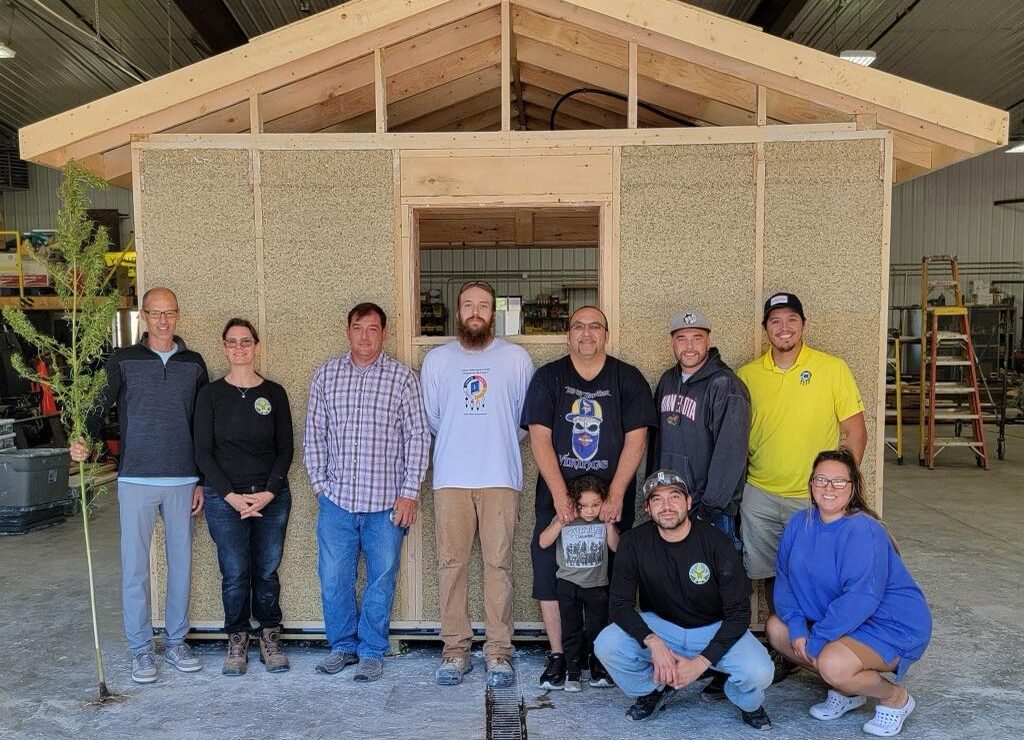 A group of people stand smiling in front of a Hempcrete house